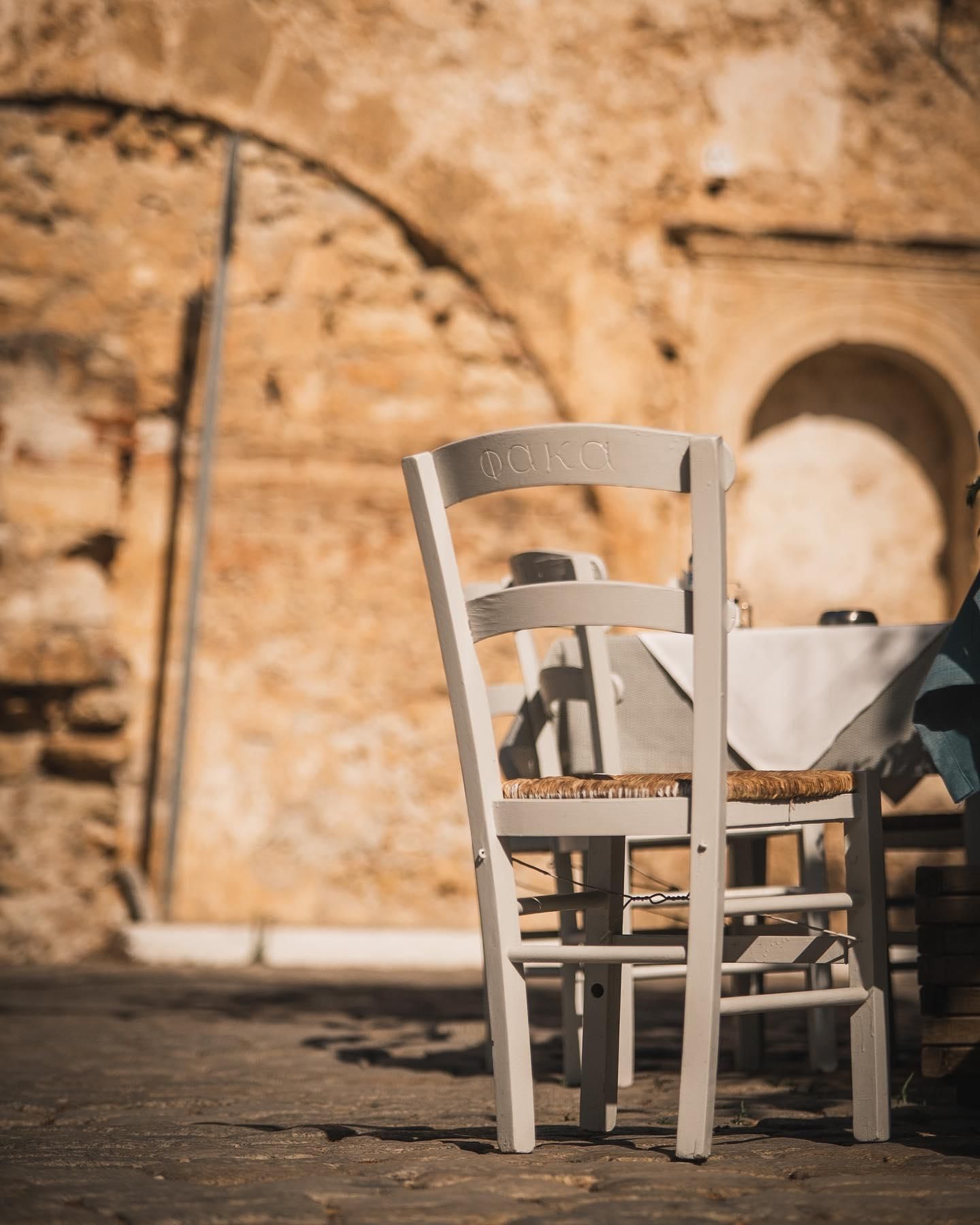 Λευκή καρέκλα με ψάθα μπροστά σε πέτρινη ενετική καμάρα.